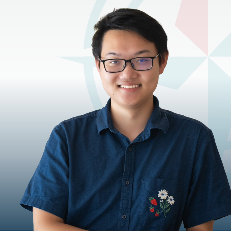 Smiling person wearing glasses and a blue shirt with floral embroidery, standing against a pastel geometric background, conveying a cheerful tone.